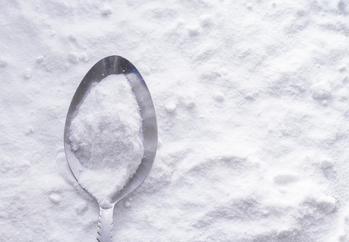 A spoon rests on a bed of white powder, possibly baking soda or flour.