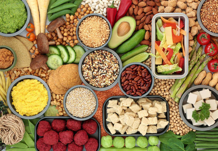 Assorted vegan foods, including vegetables, grains, beans, and tofu, arranged around various bowls and dishes.